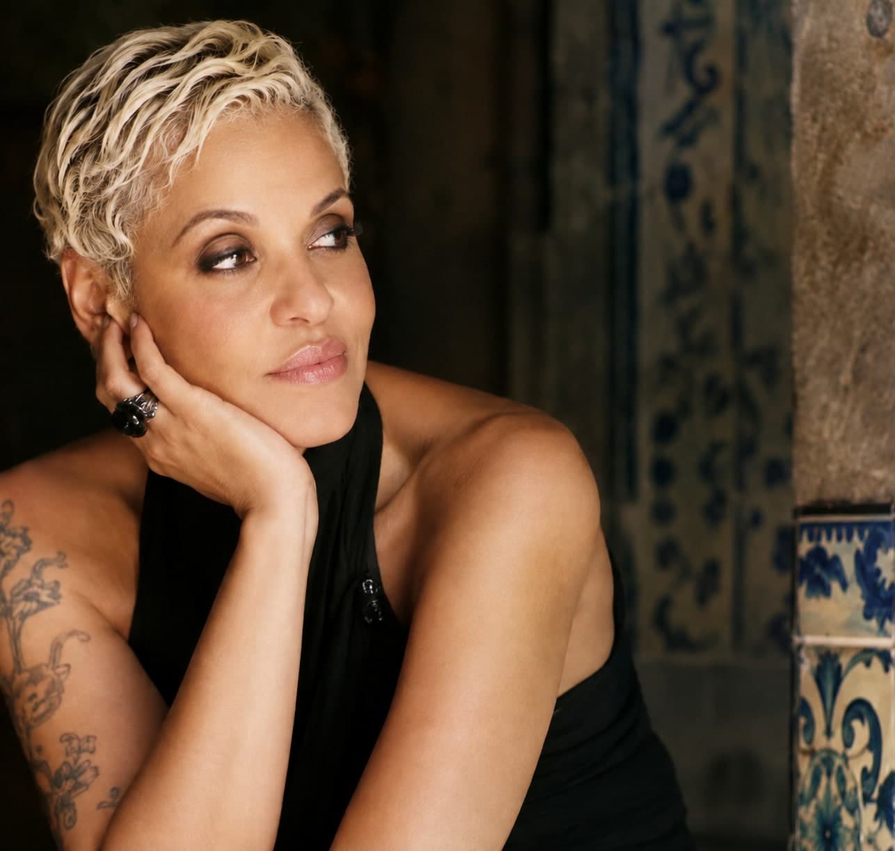 Mariza em retrato, mão apoiando o rosto, azulejo português ao fundo